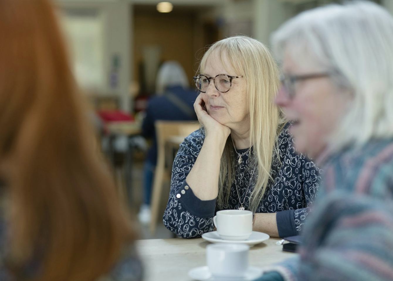 Vier vrouwen in gesprek aan tafel, met een kop koffie